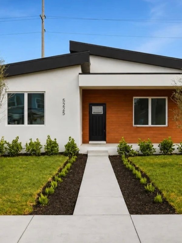 A newly built modern home with a wood-accented porch, fresh landscaping, and a front walkway