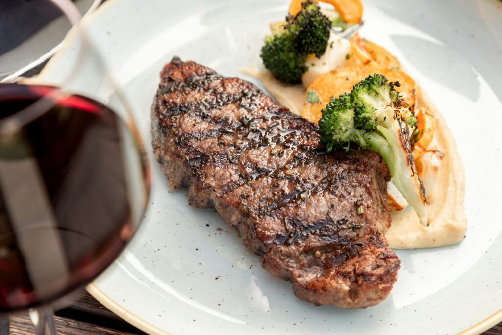 Grilled strip steak with roasted vegetables next to a glass of red wine